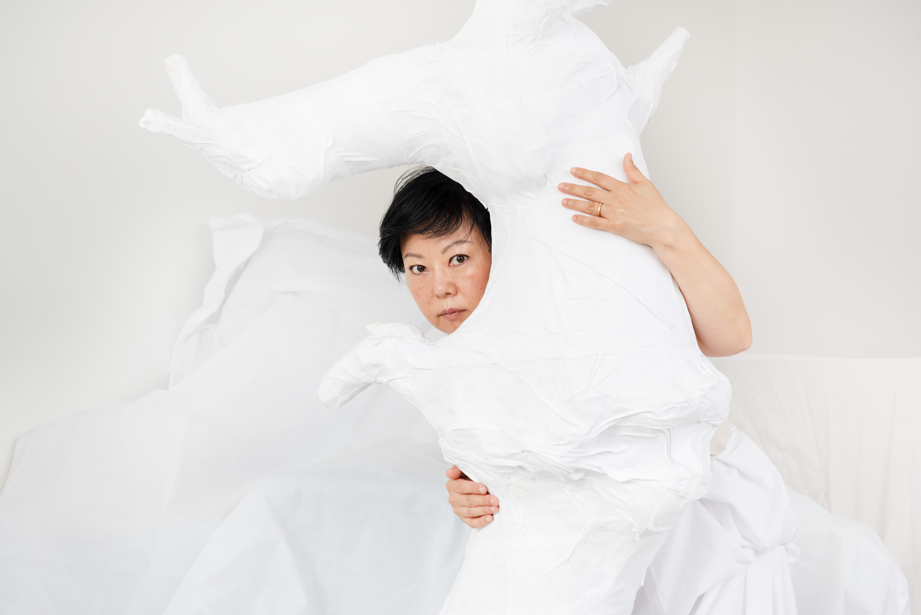 an Asian woman peeking out of a white sculpture tree trunk