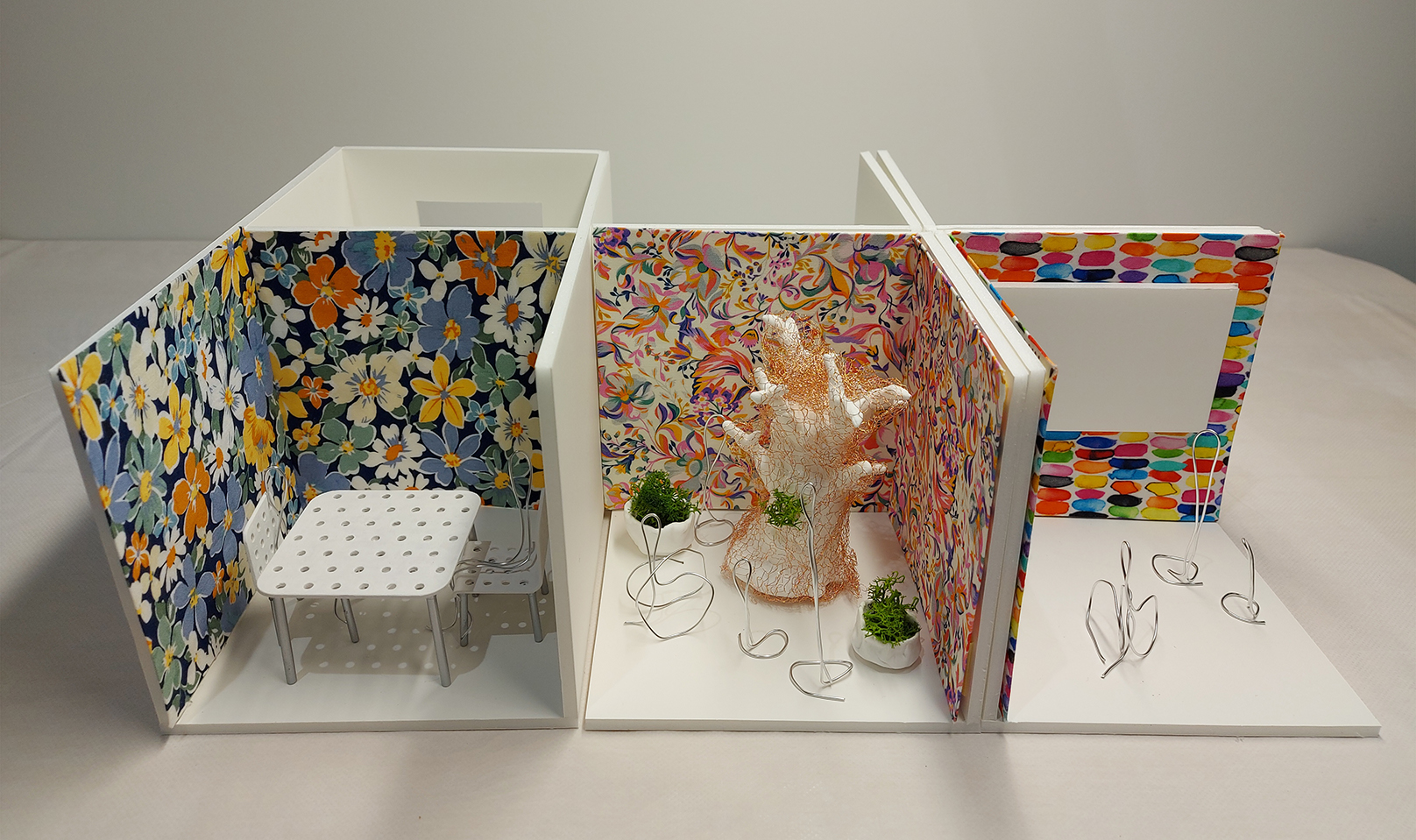 a miniature model with 6 cubicles, three at the front and three at the back. Front three has colourful walls with miniature table, white tree, and a screen.